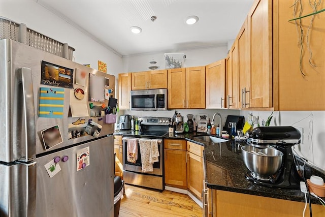 kitchen with ornamental molding, dark stone counters, a sink, light wood finished floors, and appliances with stainless steel finishes