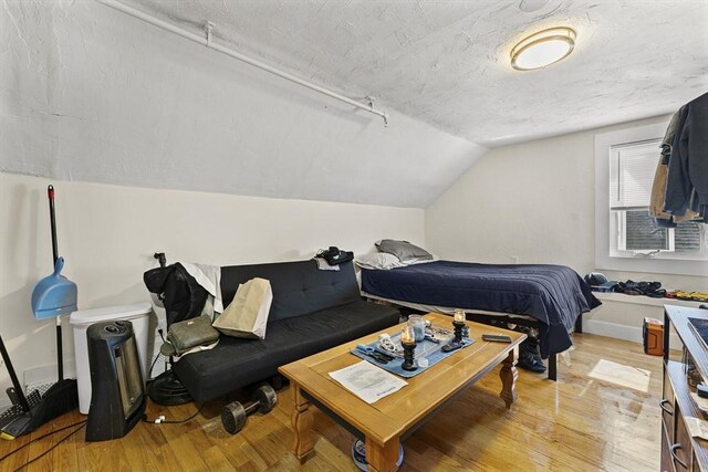 bedroom featuring light wood-style flooring, baseboards, lofted ceiling, and a textured ceiling