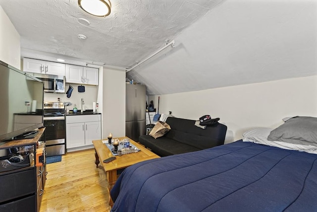 bedroom with refrigerator, lofted ceiling, a textured ceiling, freestanding refrigerator, and light wood-style flooring