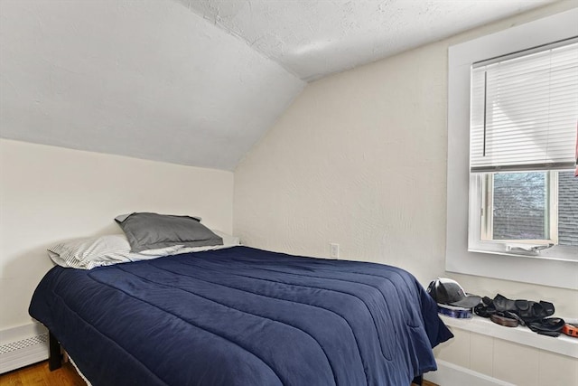 bedroom with a textured ceiling, vaulted ceiling, a baseboard heating unit, and wood finished floors