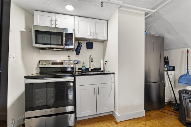 kitchen featuring white cabinets, a sink, stainless steel appliances, and light wood-type flooring