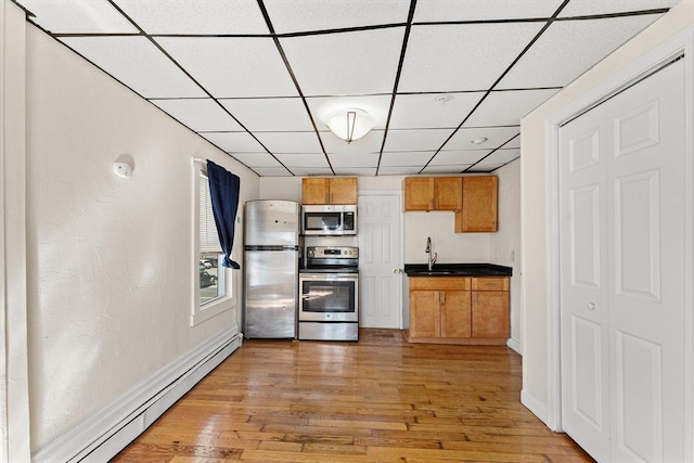 kitchen featuring light wood finished floors, stainless steel appliances, dark countertops, a sink, and a baseboard heating unit