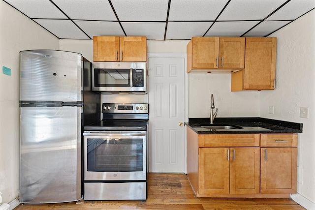 kitchen featuring a drop ceiling, a sink, stainless steel appliances, and dark stone countertops