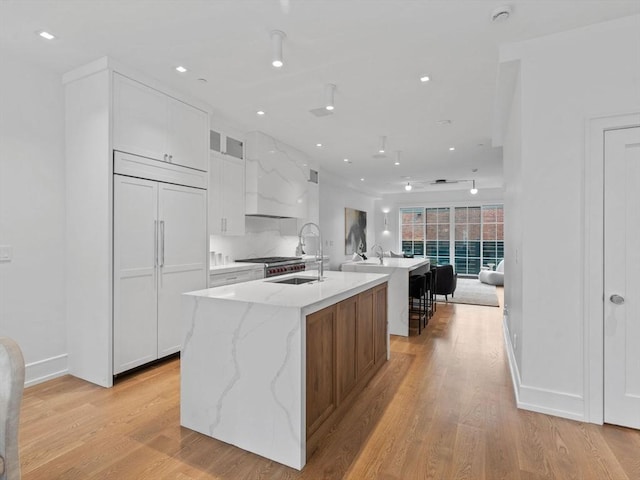 559 E Broadway Unit 559, Boston, MA 02127 - kitchen featuring a center island with sink, white cabinetry, light wood-style floors, glass insert cabinets, and recessed lighting