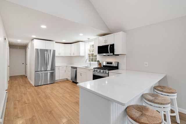 kitchen featuring light wood finished floors, a breakfast bar area, a peninsula, stainless steel appliances, and a sink