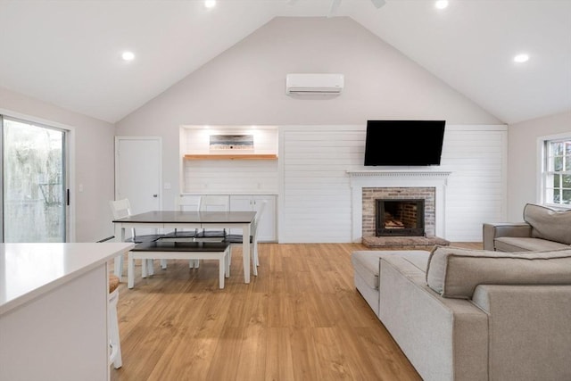 living area with a wall mounted air conditioner, high vaulted ceiling, a brick fireplace, and light wood finished floors