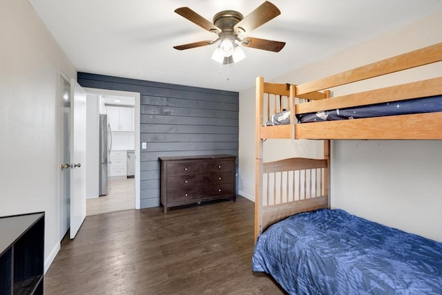 bedroom featuring wood walls, wood finished floors, a ceiling fan, and freestanding refrigerator