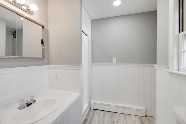 bathroom featuring wood finished floors, a sink, wainscoting, curtained shower, and baseboard heating