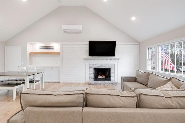 living room featuring a wall unit AC, a fireplace, light wood finished floors, and high vaulted ceiling