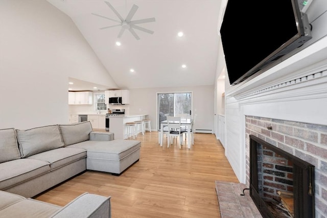 living room featuring high vaulted ceiling, light wood-style flooring, a baseboard heating unit, recessed lighting, and a brick fireplace