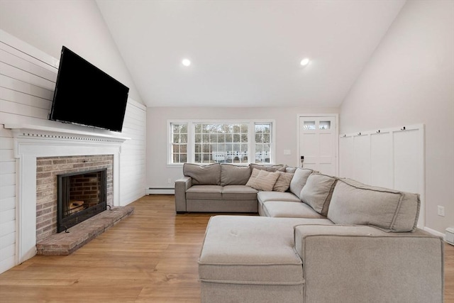 living room featuring a brick fireplace, light wood-style floors, baseboard heating, and high vaulted ceiling