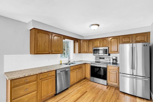 kitchen with sink, backsplash, stainless steel appliances, light stone countertops, and light wood-type flooring