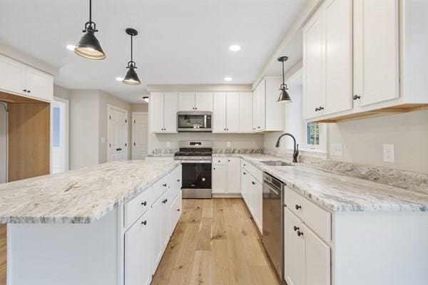 kitchen featuring a center island, a sink, white cabinetry, light wood-style floors, and appliances with stainless steel finishes