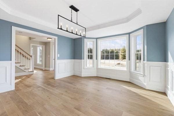 unfurnished dining area with a tray ceiling, stairway, a decorative wall, and a wainscoted wall