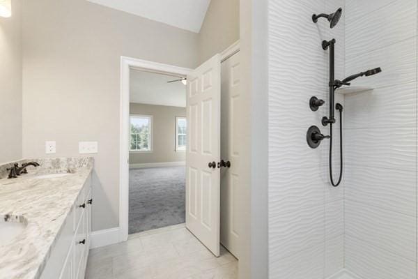 bathroom with a tile shower, double vanity, baseboards, and a sink