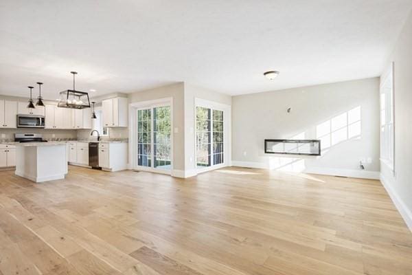 unfurnished living room with baseboards, an inviting chandelier, a sink, and light wood-style flooring