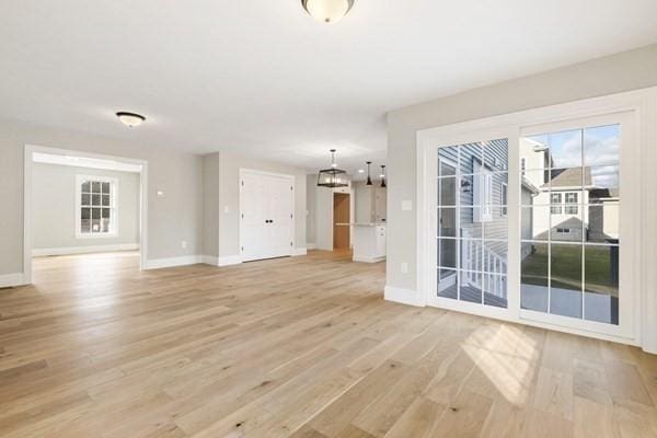 unfurnished living room with baseboards, a chandelier, and light wood-type flooring