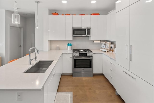 kitchen featuring appliances with stainless steel finishes, sink, white cabinets, and decorative light fixtures