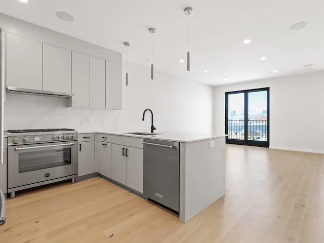 kitchen with stainless steel appliances, a sink, a peninsula, light wood-type flooring, and light countertops