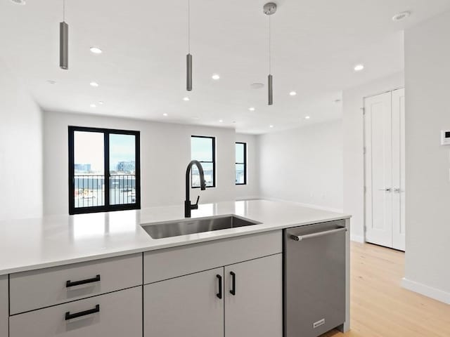 kitchen with a sink, stainless steel dishwasher, open floor plan, light wood-style flooring, and light countertops