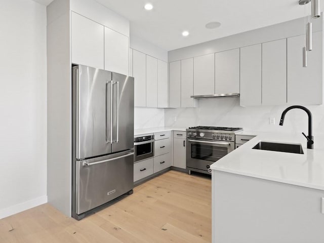 kitchen featuring premium appliances, a sink, light wood finished floors, recessed lighting, and light countertops