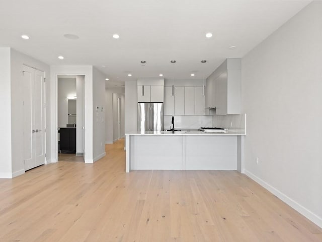 kitchen with stainless steel refrigerator, a sink, baseboards, light countertops, and recessed lighting