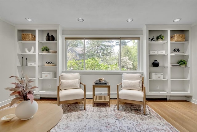sitting room with a baseboard radiator, wood finished floors, and ornamental molding