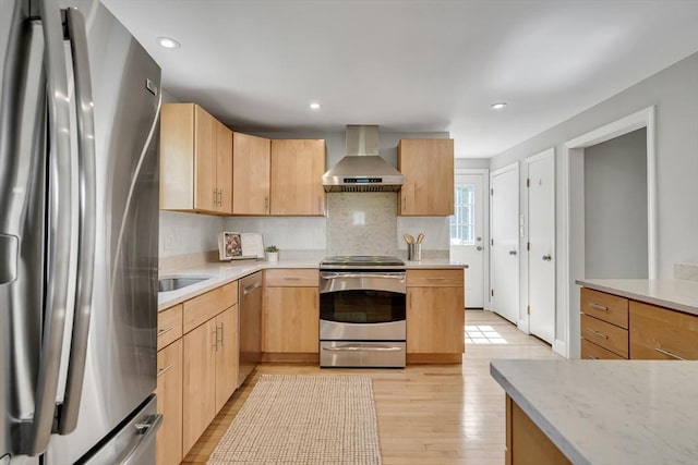 kitchen featuring appliances with stainless steel finishes, light brown cabinets, light wood-type flooring, and wall chimney exhaust hood