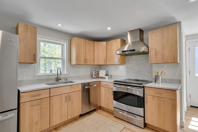 kitchen with light brown cabinetry, stainless steel appliances, a sink, and wall chimney exhaust hood