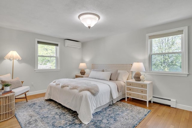 bedroom with baseboards, a wall mounted AC, baseboard heating, and hardwood / wood-style flooring