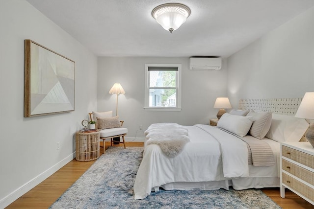 bedroom with baseboards, a wall unit AC, and wood finished floors
