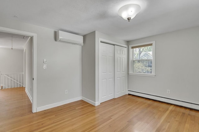 unfurnished bedroom featuring light wood-type flooring, attic access, a baseboard heating unit, and a wall unit AC