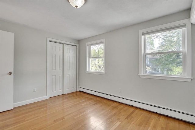 unfurnished bedroom featuring light wood-style floors, an AC wall unit, baseboard heating, and a closet