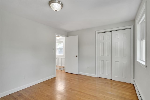 unfurnished bedroom with baseboards, baseboard heating, light wood finished floors, and a closet