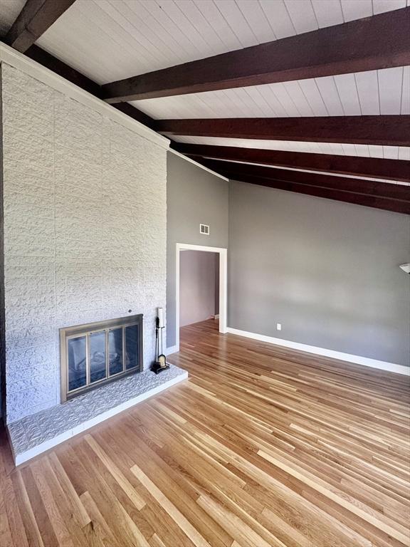 unfurnished living room featuring baseboards, beamed ceiling, light wood finished floors, and a large fireplace