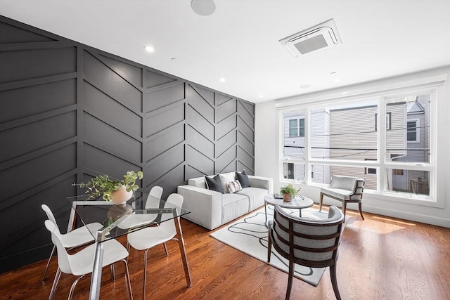 living room with a decorative wall, recessed lighting, wood finished floors, and visible vents
