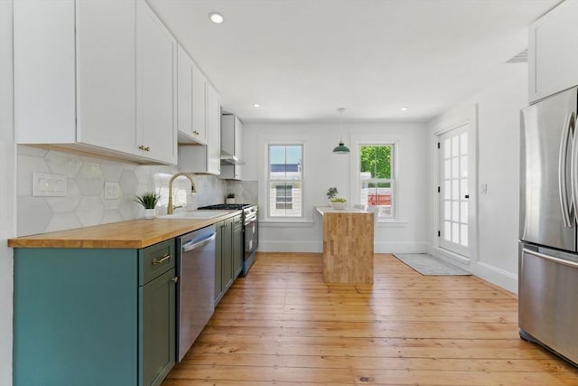 kitchen featuring appliances with stainless steel finishes, a sink, light wood finished floors, butcher block counters, and recessed lighting