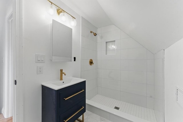 bathroom featuring lofted ceiling, a tile shower, and vanity