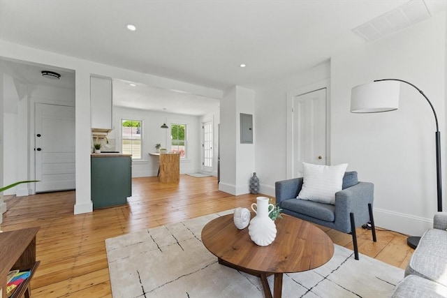 living area with light wood-type flooring, recessed lighting, electric panel, and baseboards