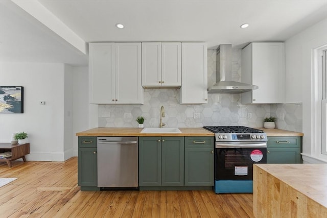 kitchen featuring appliances with stainless steel finishes, wall chimney exhaust hood, a sink, green cabinets, and wooden counters