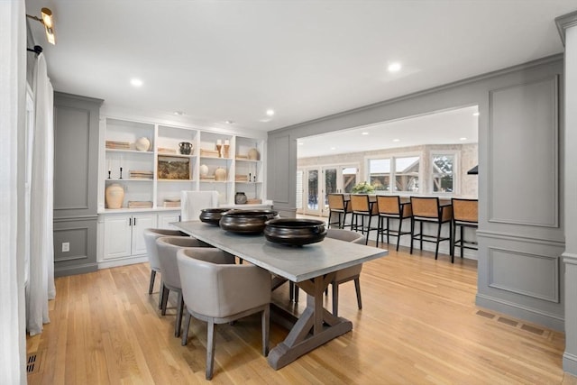 dining room with light wood-style flooring, a decorative wall, and recessed lighting