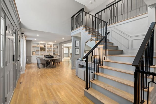 entrance foyer featuring a towering ceiling, stairway, light wood-style floors, a decorative wall, and recessed lighting