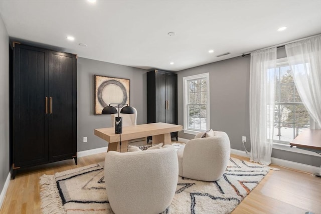 office area with light wood-type flooring, a wealth of natural light, visible vents, and baseboards