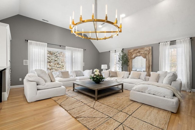 living area featuring a chandelier, high vaulted ceiling, wood finished floors, visible vents, and baseboards