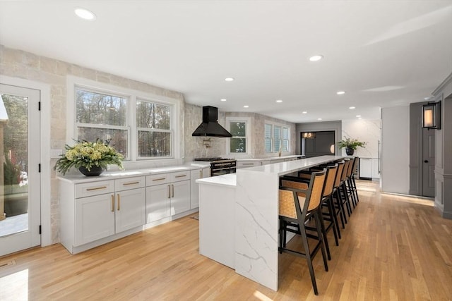 kitchen with light wood-style flooring, white cabinets, wall chimney range hood, high end range, and a kitchen bar