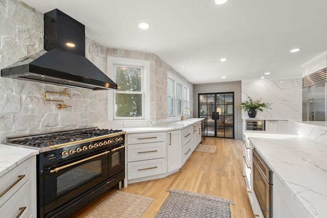 kitchen featuring tasteful backsplash, white cabinets, premium appliances, wall chimney exhaust hood, and light stone countertops