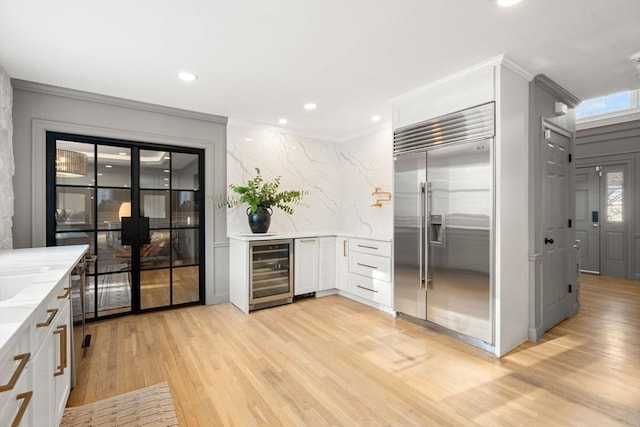 kitchen featuring beverage cooler, white cabinets, stainless steel built in fridge, light wood-type flooring, and backsplash