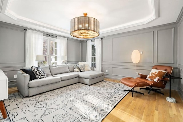 living room featuring ornamental molding, a raised ceiling, a decorative wall, and light wood-style flooring