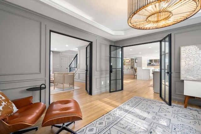 interior space with crown molding, a raised ceiling, a decorative wall, stairway, and light wood-style flooring