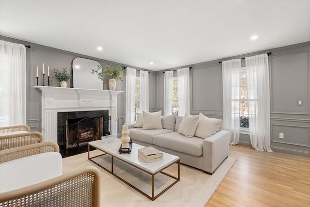 living area with light wood finished floors, a tile fireplace, crown molding, a decorative wall, and recessed lighting